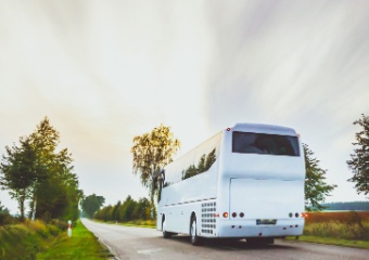 the back of a plain white charter bus as it drives down a rural road in Texas