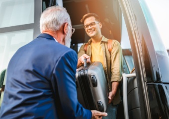two people move a piece of luggage onto their charter bus rental