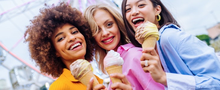 three friends enjoy ice cream together at a fair